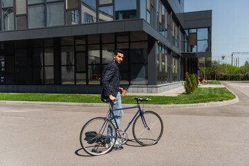 Fototapeta na wymiar Arabian businessman holding paper cup near bike on urban street
