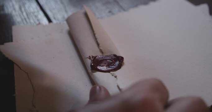 Hands Putting Pressure on a Stamp as It Seals a Paper With Red Wax
