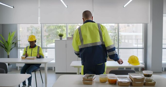 Group of young industrial workers eating takeaway lunch at modern office canteen