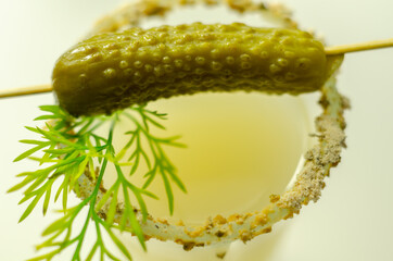 Close up of a drink based on vodka and cucumber juice in a shot glass decorated with small pickled cucumber and dill