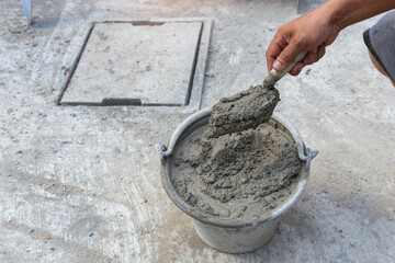 Hand hold a trowel and bucket with cement mixed in construction site