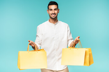 Positive arabian man holding yellow shopping bags isolated on blue