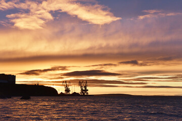 Silhouettes of cranes in the sea port against summer sunset