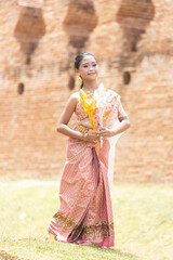 A long-haired Asian schoolgirl dressed in traditional Thai costumes holding silver and gold flowers in a dance performance.