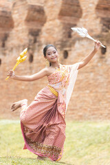 A long-haired Asian schoolgirl dressed in traditional Thai costumes holds silver and gold flowers and performs dance moves.
