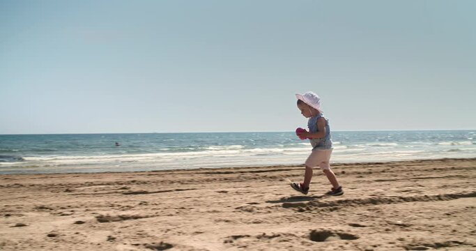 Young little baby girl running on empty beach one sunny summer day with sea view