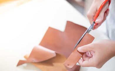 Female hand cutting the leather plate with pattern standard size, The leather for tag or keychain.