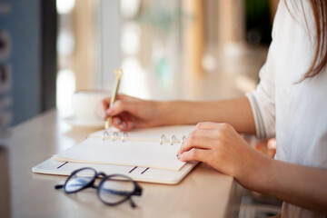 Young businesswoman in eyeglasses planning and writing down the daily schedule with in agenda