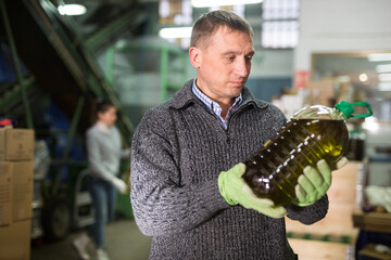 Focused man engaged in family production of olive oil inspecting quality of bottled oil at warehouse