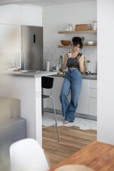 Pleasant domestic woman relaxing at modern kitchen chatting use smartphone white cuisine interior