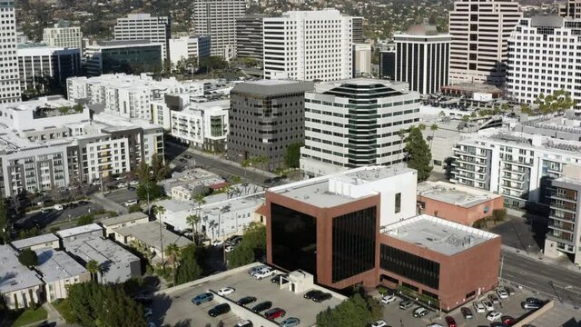 Aerial Moving Forward Over A Sunny Downtown City Skyline With Bright Sunlight, White Towers, And Rugged California Mountains On The Horizon - Glendale, California