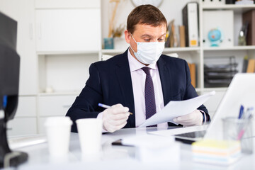 Focused businessman in disposable face mask and rubber gloves working in office. Necessary precautions during COVID 19 pandemic