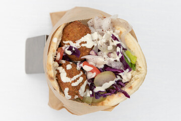 Overhead view of pita wrap sandwich loaded with meat, bite size falafels, and vegetable fillings...