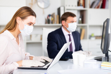 Office workers in protective medical masks work at the computer
