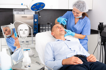 Obraz premium Skilled woman beautician filling males wrinkles using rejuvenating injections in clinic of aesthetic medicine