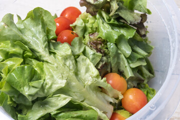 Salad vegetables, tomatoes in a plastic bowl, organic system, healthy food, on a wooden floor.