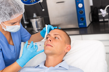 Young adult man patient of cosmetologist receiving hyaluronic acid injections