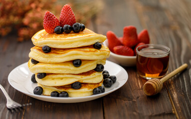 Sweet food. Stack of delicious pancakes with blueberries, Strawberry and honey in white plate on blur wooden background.
