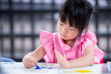 Pupil kid learning art on white paper with chalk color. Study at home. Asian child doing crafting on the table. Happy cute girl wearing pink t-shirt aged 4 years old.