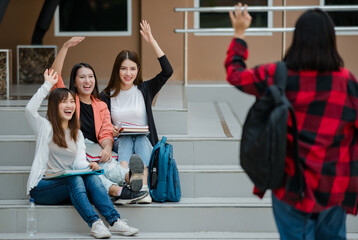 Group of three attractive asian college students sitting down on staircases in university campus waving hello to their friends outdoor. Concept for education, friendship and college students life © Bangkok Click Studio