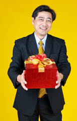 Adult man look at camera standing with give gift, red box.  Seems have a lot of value to someone. Yellow background makes image bright and a fun mood suitable for celebration.
