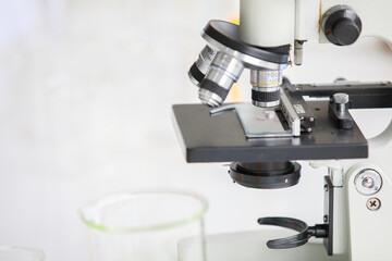 Closeup shot of microscope lens and sample on glass plate in laboratory room with colorful reagent in tube and beaker in blurred foreground and background