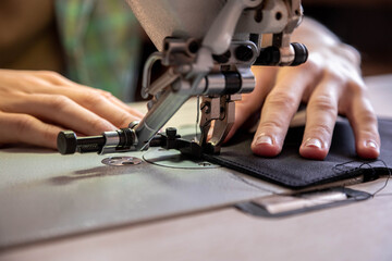 Close up craftsman hands sew stuff blank for wallet use sewing machine. Working at leather workshop