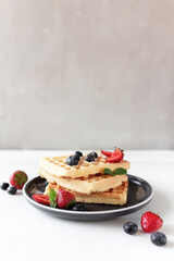 Stack of waffles on plate on table with blueberry, strawberry and mint leaves