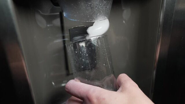 This video shows a refrigerator's ice machine filling a glass cup with ice cubes in slow motion.