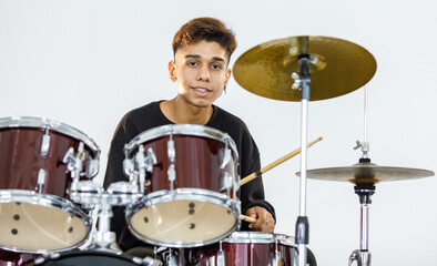 Fototapeta na wymiar Front view portrait shot of a teenage drummer playing the music. Young musician playing the drum while looking at the camera and smiling. Junior student playing an instrument with white background