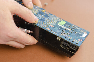 Graphics card on a brown background. Man disassembles computer components, unscrewing screws....
