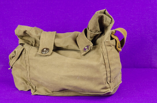 Old Army gas mask in canvas pouch with lilac background. Personal protection against chemical and radiological weapons as well as poisonous gases in a green carrying bag.
