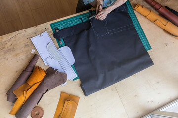 Craftsman drawing scheme lining for bag on tissue creating leatherwork at studio leather workshop