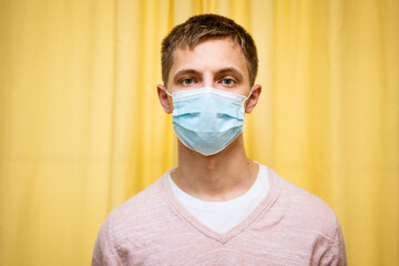 a young guy of Caucasian appearance in casual clothes on a yellow background in a protective mask looks at the camera