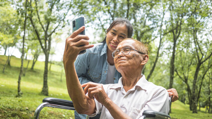 Grandfather in wheelchair and granddaughter talking video call with relatives via smartphone in...