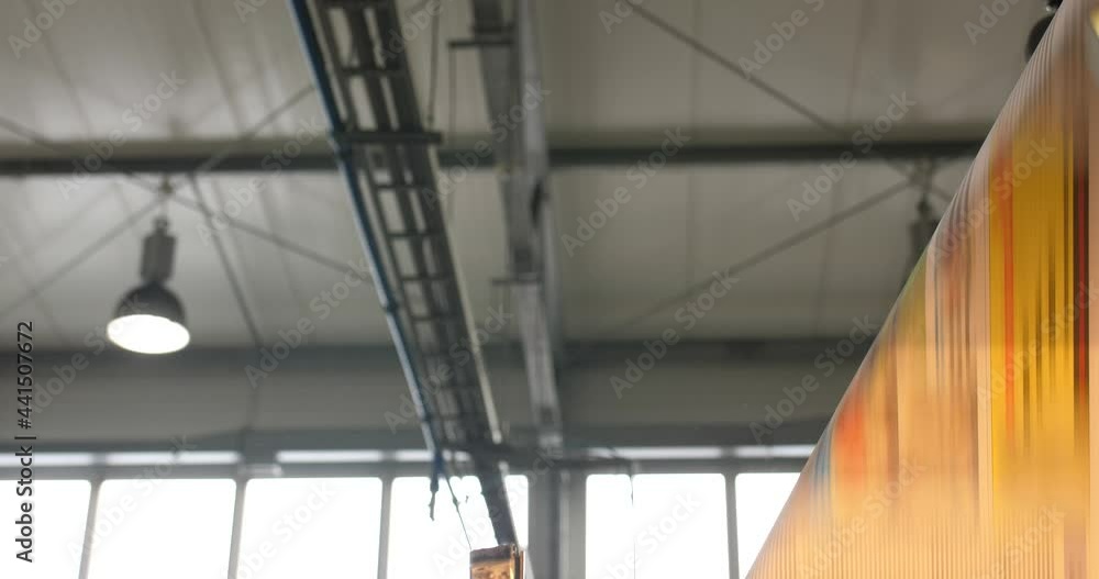 Poster printed paper streamed over roll machine in factory printworks with ceiling of building visible and 