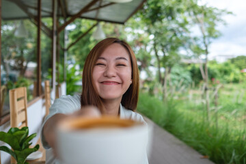 A young asian woman holding and showing a cup of coffee in the outdoors cafe