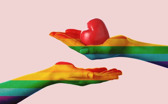 Female hands painted in colors of LGBT flag with heart on pink background