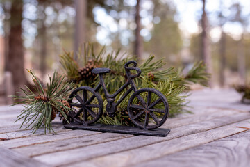Small isolated decorative metal bike on a wooden deck next to pine branches