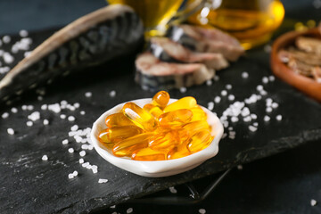 Bowl with fish oil pills on dark background