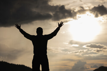 Fototapeta na wymiar Silhouette Young man raised hand in the air with success goal on sunset background. Man standing on top of the mountain freedom life concept.