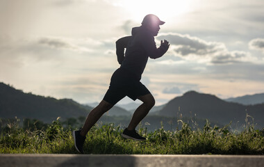 Silhouette Young man wearing sportswear running outdoor nature mountain background. Man jogging on the country side road. Training athlete outdoor concept.