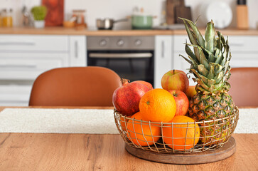 Basket with fresh fruits on wooden table in kitchen
