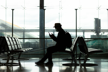 silhouette of young travel backpack using smartphone in the Passenger Departure Arrival building in the airport. He travel alone in station.