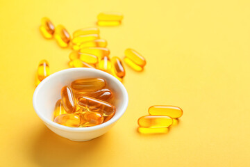 Bowl with fish oil capsules on color background