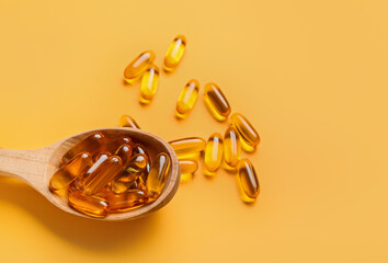 Spoon with fish oil capsules on color background