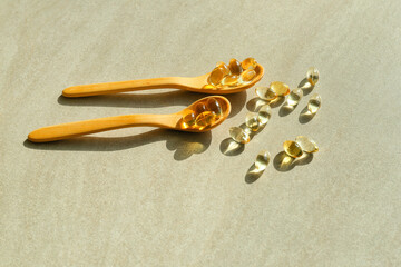 Spoons with fish oil capsules on grey background