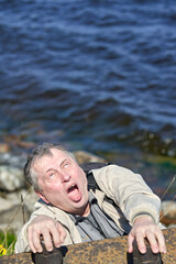 Freak clings his hands to the edge of the cliff above the water