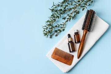 Hair brush, comb, towel and bottles of essential oil on color background