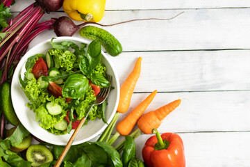 Plate of fresh summer salad on a wooden white table, top view, copy space. Clean and healthy food background